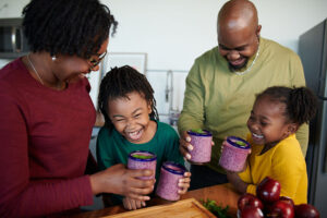A mom, dad, and two girls in a kitchen enjoying smoothies.