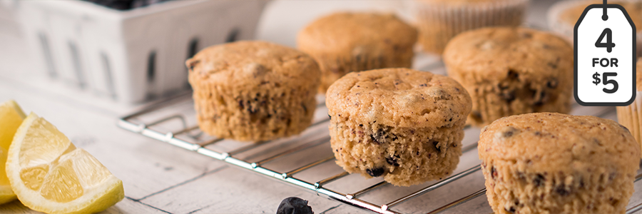 Close up of muffins on a cooling rack. A pint of fresh blueberries is blurred in the background.