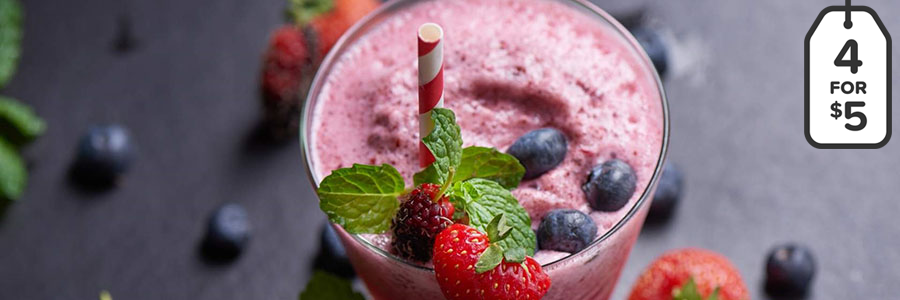 Wide shot of a pink-colored smoothie garnished with blueberries, strawberries, and a red and white striped straw.
