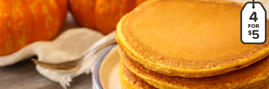 Close up shot of a stack of four pumpkin pancakes with two small pumpkins blurred in the background.