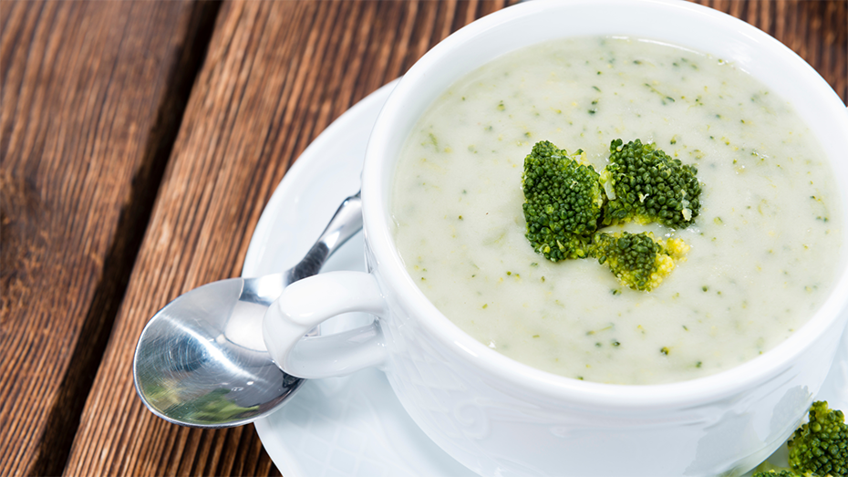 Bowl of broccoli cheddar soup, garnished with broccoli florets.