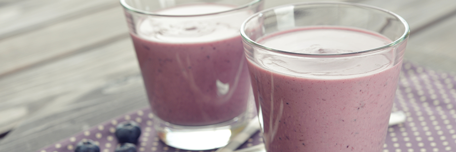 Two blueberry smoothies in short glasses on a table.