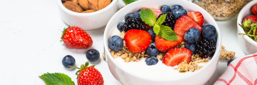 Bowl with yogurt, topped with strawberries, blueberries, and granola. Garnished with a sprig of mint.