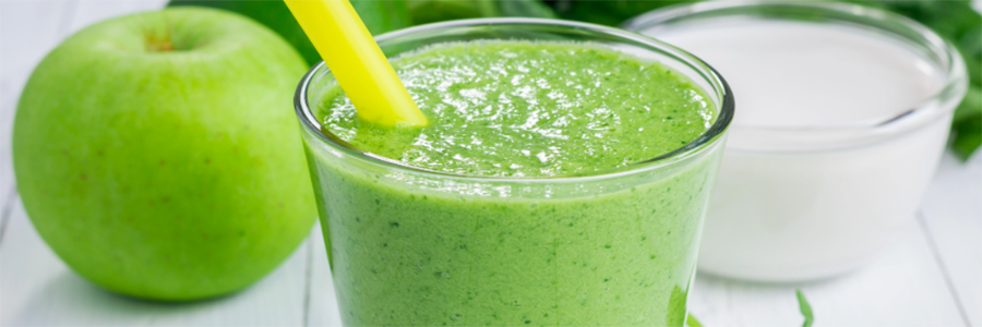 Small glass with a green smoothie with a yellow straw. Smoothie is displayed with a Granny Smith apple on the table.
