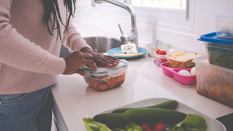 A woman in a kitchen putting the lid on a container of leftovers.