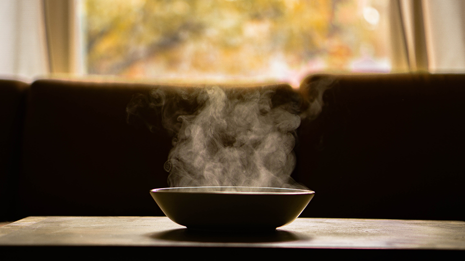 Silhouette of a bowl of hot steaming soup sitting on a table.