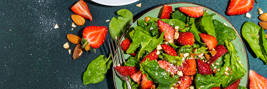 Overhead shot of salad with baby spinach and sliced strawberries. Salad is garnished with poppy seeds.