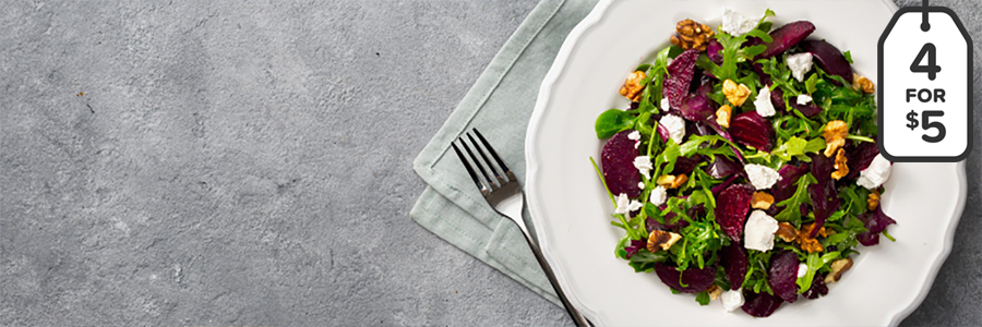 Arugula greens topped with sliced red beats, walnuts, and feta cheese on a white round plate.