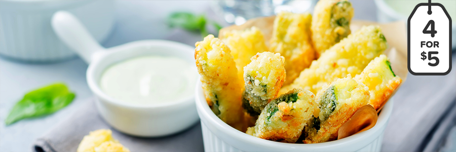 Close shot of zucchini-shaped fries that have been coated in breadcrumbs and Parmesan cheese. Fries are displayed in a white ramekin.