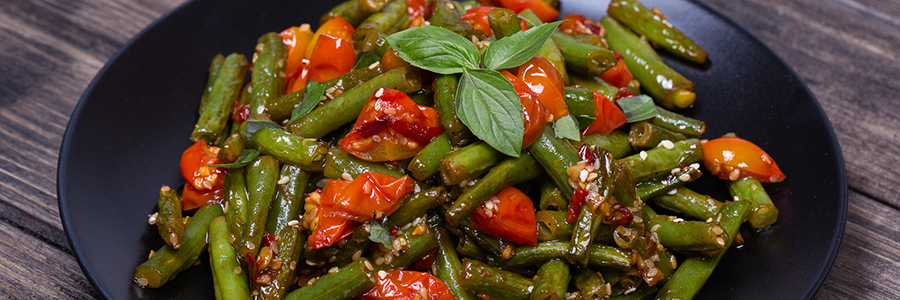 Plate of sauteed green beans with cheery tomatoes, and red peppers.