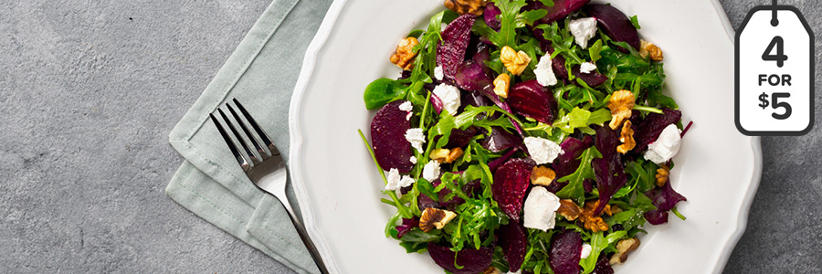Arugula greens topped with sliced red beats, walnuts, and feta cheese on a white round plate.