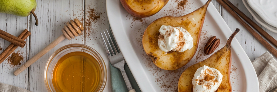 Overhead shot of a platter with baked pears topped with yogurt and garnished with cinnamon. Platter is displayed with a bowl of honey and honey dipper.
