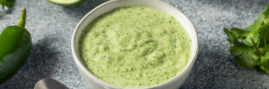 Bowl of green goddess dressing in a bowl. Herbs are displayed next to the bowl on a dining table.