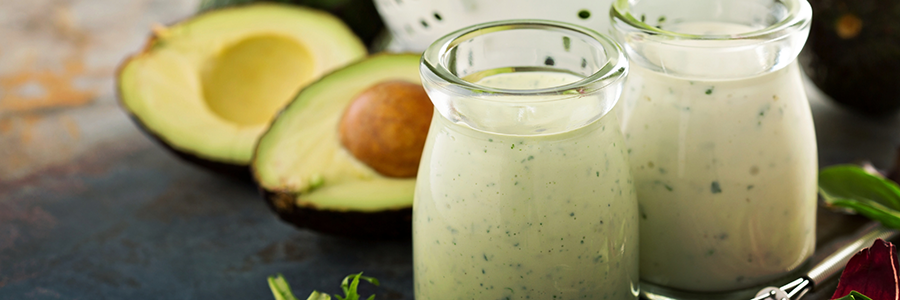 Wide shot of two small carafes with ranch dressing displayed with an avocado cut in half.