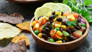 Bowl of salsa with black beans, corn, peppers, and tomatoes. Garnished with lemon slices.