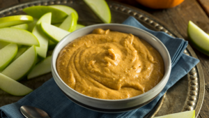 Creamy pumpkin dip in a bowl with sliced green apples displayed next to it.