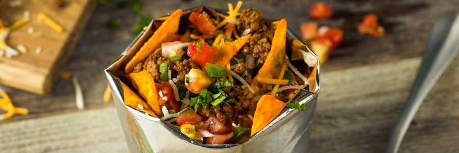 Wide shot of a bag of tortillas chips topped with ground taco meat, salsa, cheese, and cilantro.
